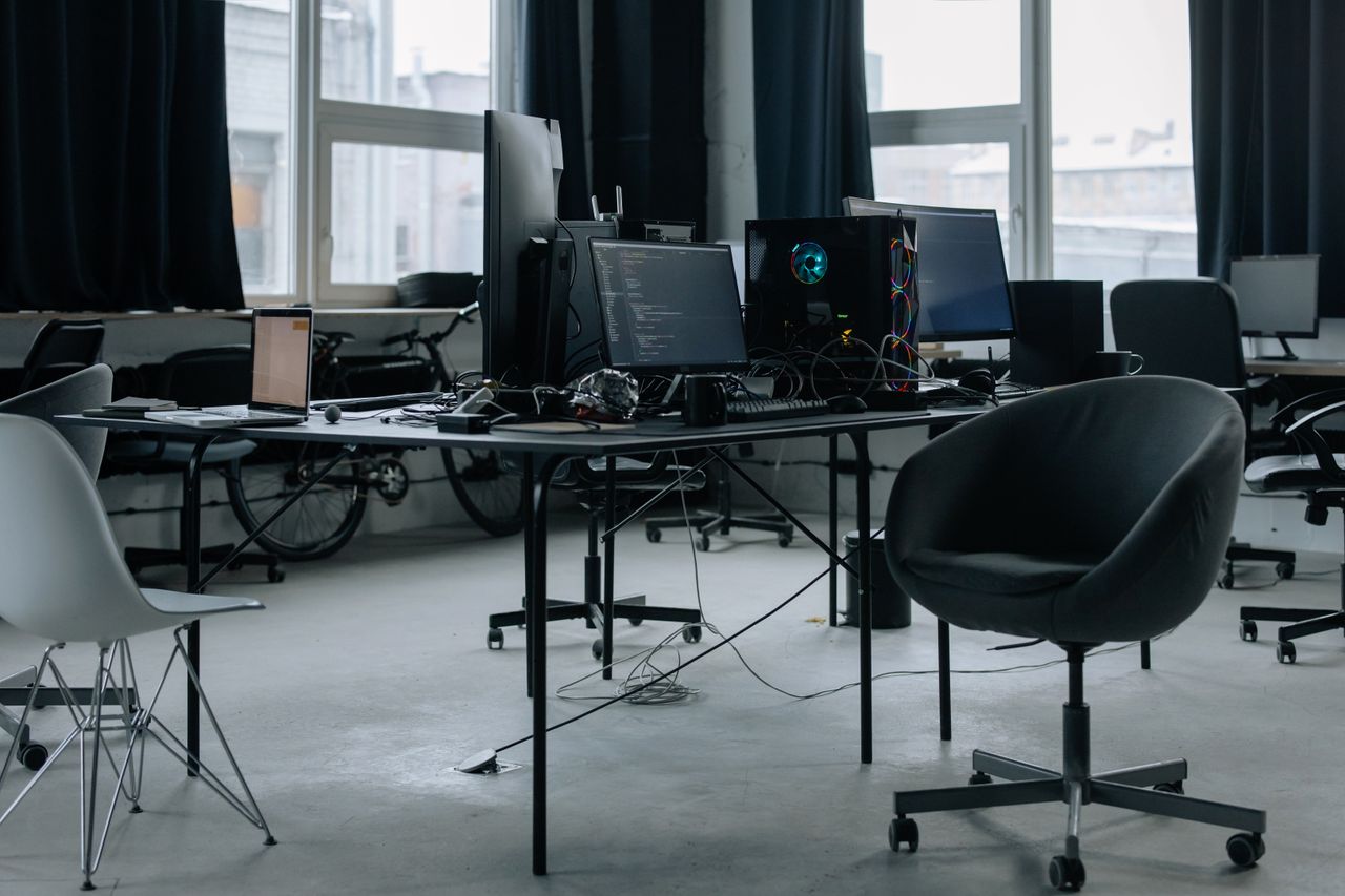 Discover a modern office workspace with computers, chairs, and natural light from large windows.